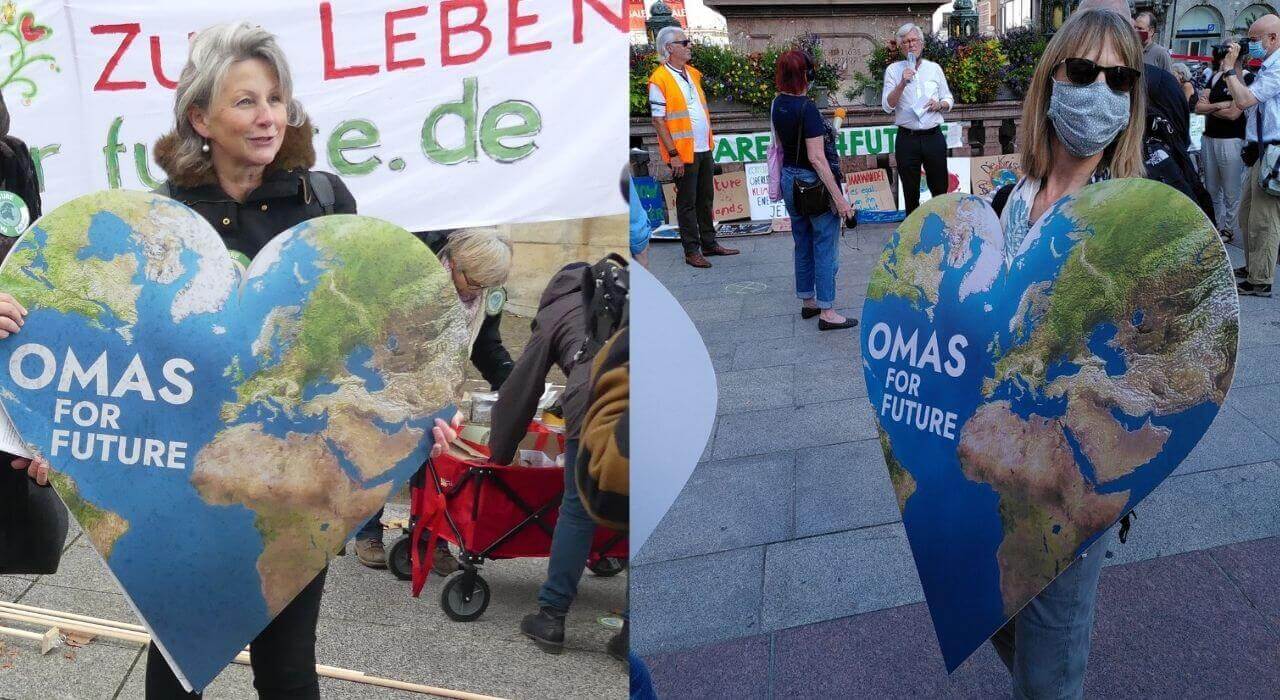 Zwei Frauen halten ein Schild in Herzform, darauf abgebildet eine Weltkarte und die Aufschrift Omas for Future.